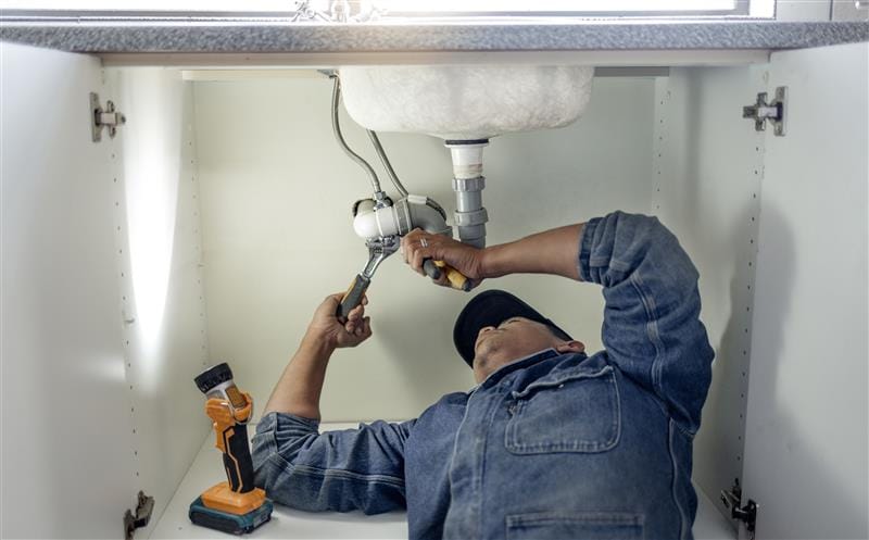 Plumber repairing pipes beneath a bathroom sink in Firestone