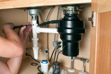 Plumber repairing a garbage disposal beneath a kitchen sink in Firestone