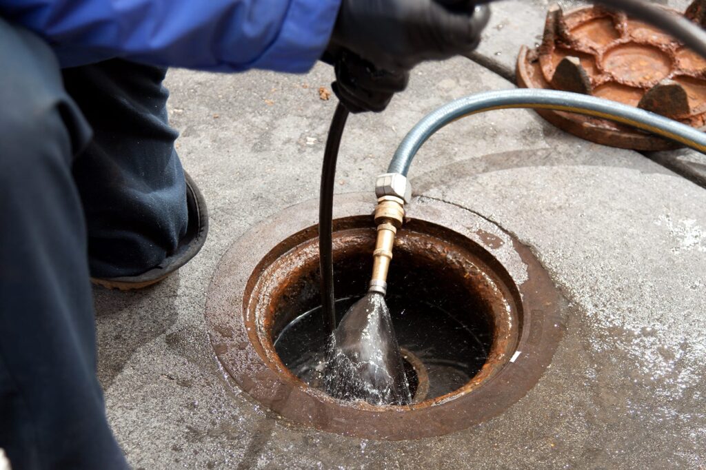 Plumber hydro jetting a sewer line through a manhole in Firestone