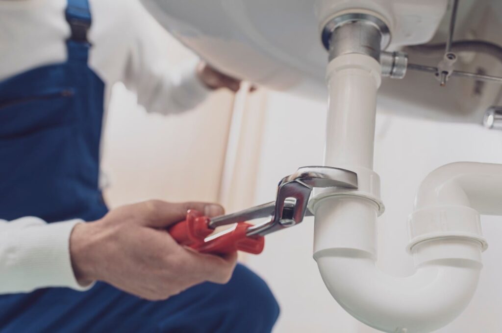 Plumber repairing a white drain pipe beneath a sink in Firestone