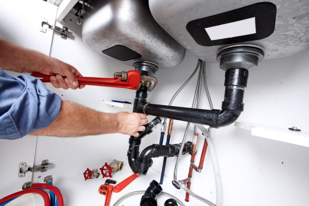 Plumber repairing drain pipes beneath a kitchen sink in Firestone