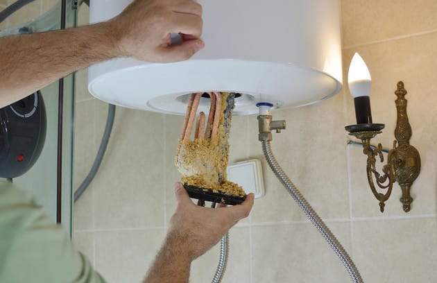 Technician removing mineral buildup from a water heater in Firestone